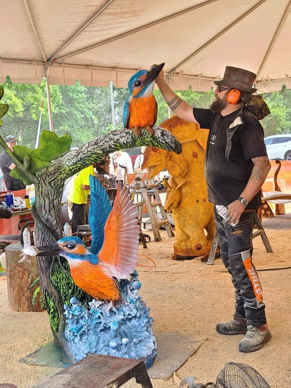 A finished chainsaw sculpture of a kingfisher diving toward water, painted in blue and orange.