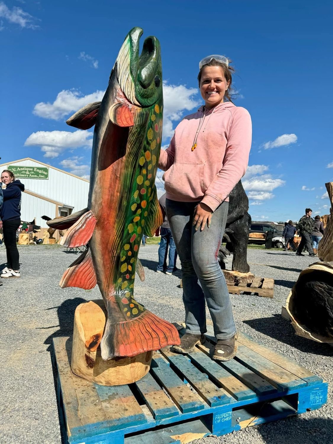 A large carved and painted trout sculpture standing upright beside the artist.