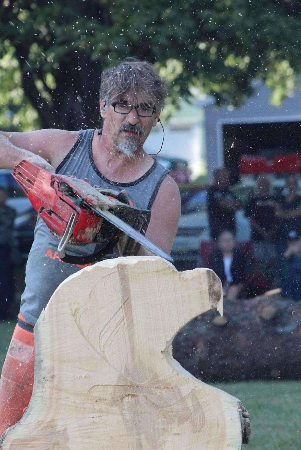 A carver cutting the rough shape of a bear from a block of wood with a red chainsaw.