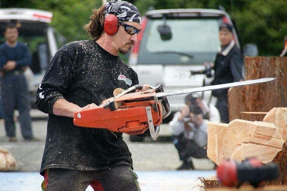 A carver leans into a log with an orange chainsaw as sawdust sprays.